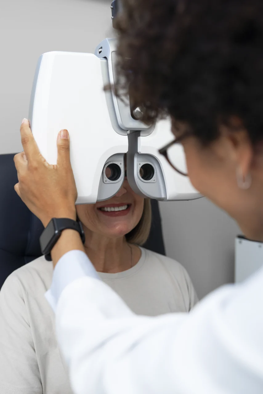 Paciente sorrindo durante exame de visão no refrator, em consulta oftalmológica